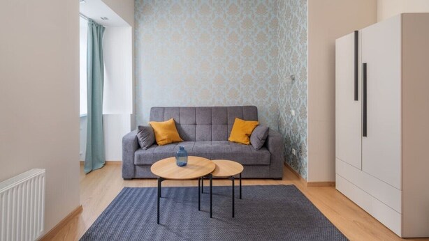 Ein modernes Wohnzimmer mit einem grauen Sofa, zwei runden Holztischen, einer gemusterten Tapete und einem weißen Schrank.