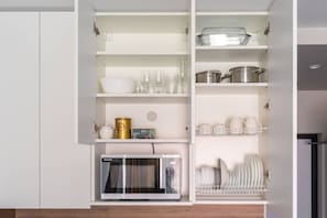 A kitchen with white cabinets, a microwave, and various kitchenware including dishes, glasses, and a coffee machine.