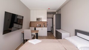 Een kleine hotelkamer met een bed, bureau, kitchenette en spiegel.