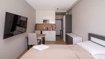 A compact hotel room with a bed, a desk, a kitchenette, and a mirror.