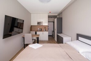Habitació d'hotel compacta amb llit, escriptori, petita cuina i mirall.