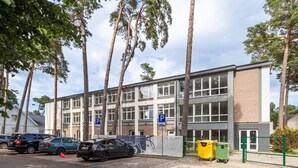 Een meerlaags gebouw met een parkeerplaats, bomen en een groene hek.