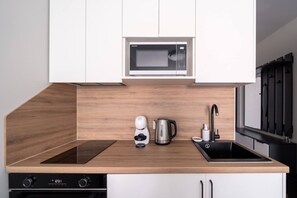 A modern kitchen with a microwave, coffee machine, kettle, and a sink.