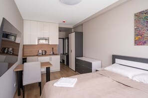 A compact hotel room with a bed, a desk, a kitchenette, and a bathroom.