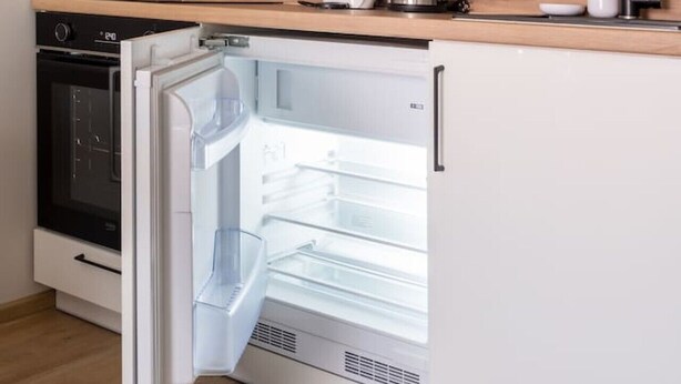 Een kleine keuken met een ingebouwde magnetron, een koffiezetapparaat, een waterkoker en een koelkast.
