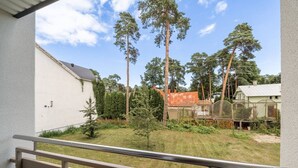 Een balkon met uitzicht op een gazon, hoge bomen en een omheind gebied met een gebouw op de achtergrond.