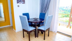 A dining area with a round table and four chairs, a window with curtains, and a view of greenery outside.