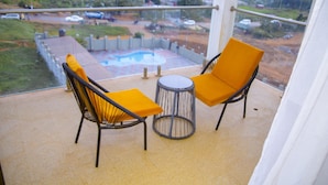 A balcony with two chairs and a small table, overlooking a swimming pool and a residential area.