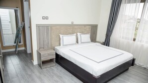 A modern bedroom with a large bed, a nightstand, and a window with curtains.