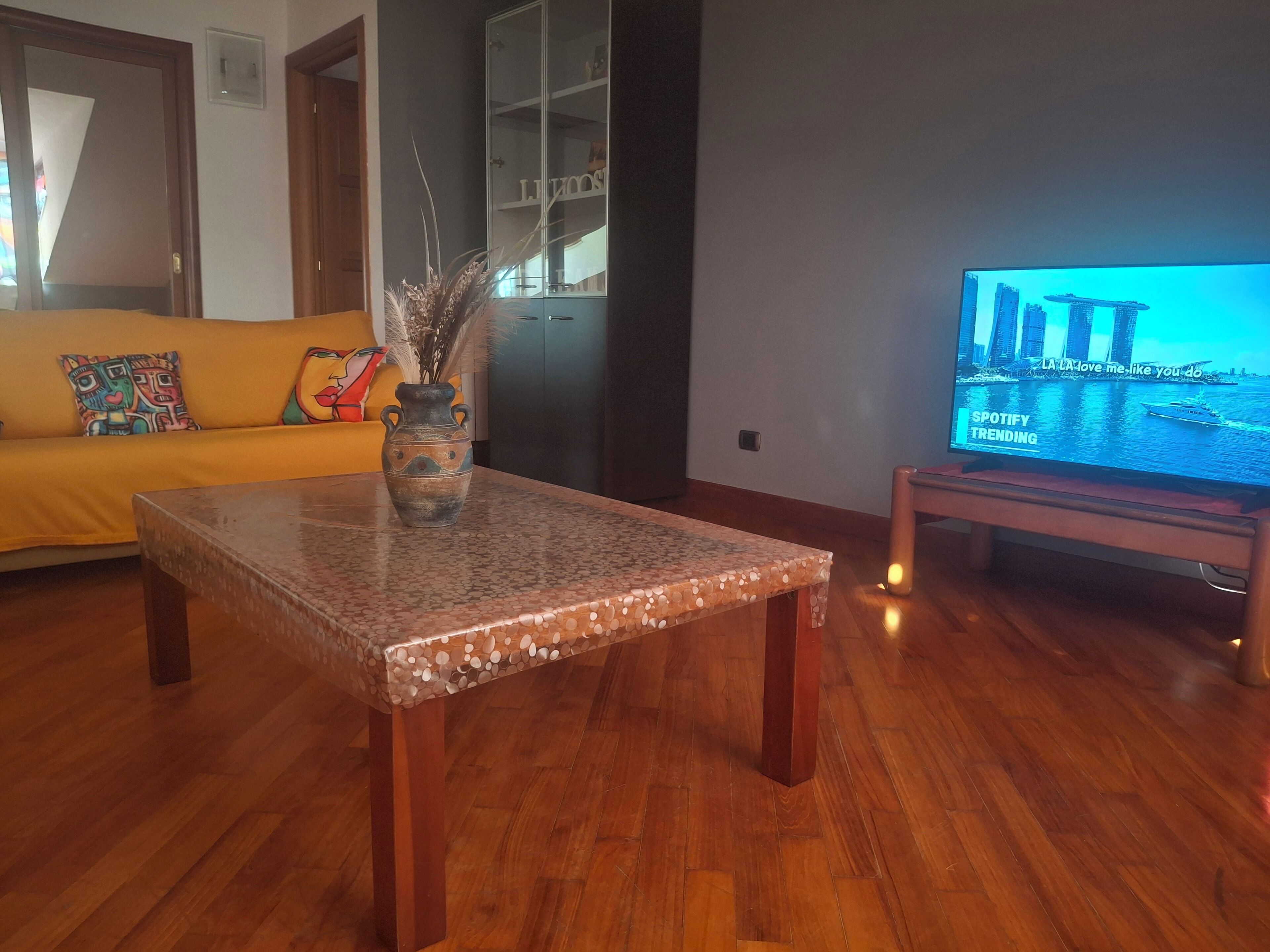 Un soggiorno con un tavolino in legno, un divano e una televisione che mostra una vista sulla città.