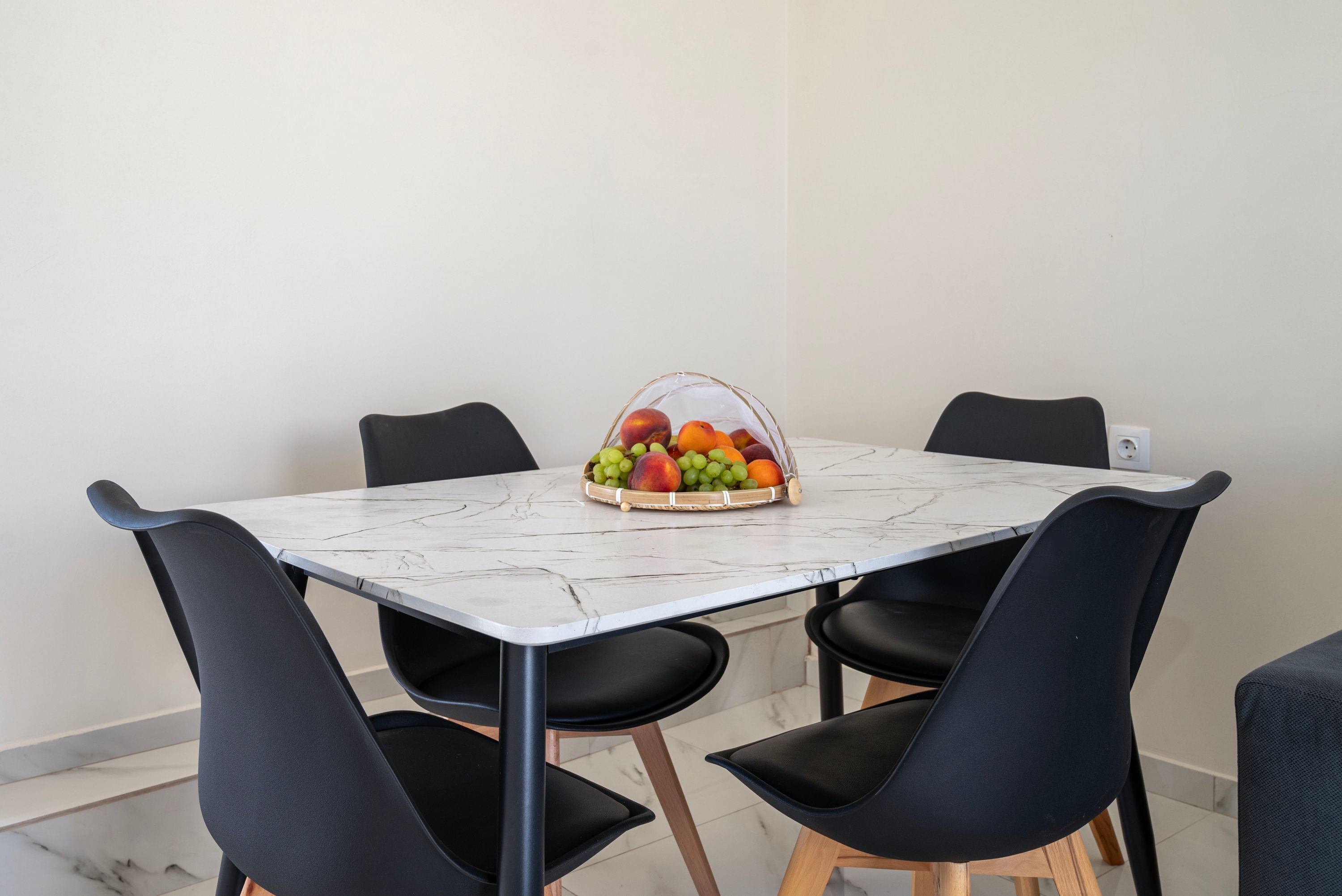 Une table à manger avec un plateau en marbre, entourée de quatre chaises noires aux pieds en bois.