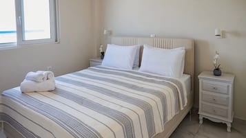 Een opgemaakt bed met een gestreept dekbed, een nachtkastje met een lamp, en een raam met jaloezieën.
