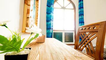 Ein Holztisch mit einem Blumentopf, ein Stuhl mit Rückenlehne aus Holz und ein Fenster mit blauen Vorhängen.