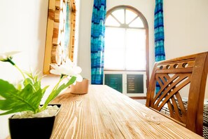 Taula de dinar de fusta amb una planta en test, una cadira amb respatller de fusta i una finestra amb cortines blaves.