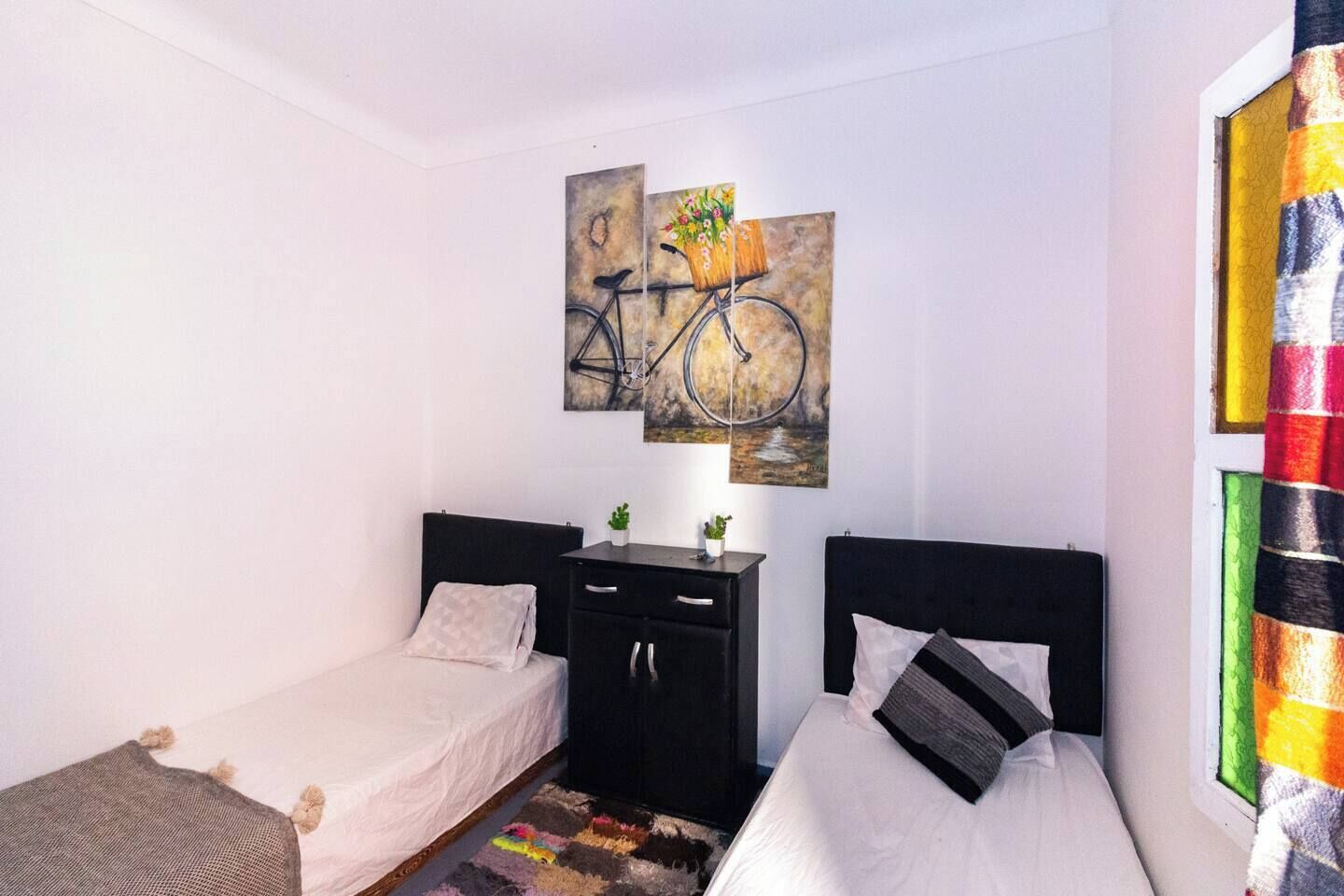 A bedroom with two beds, a nightstand, and a wall-mounted painting of a bicycle.