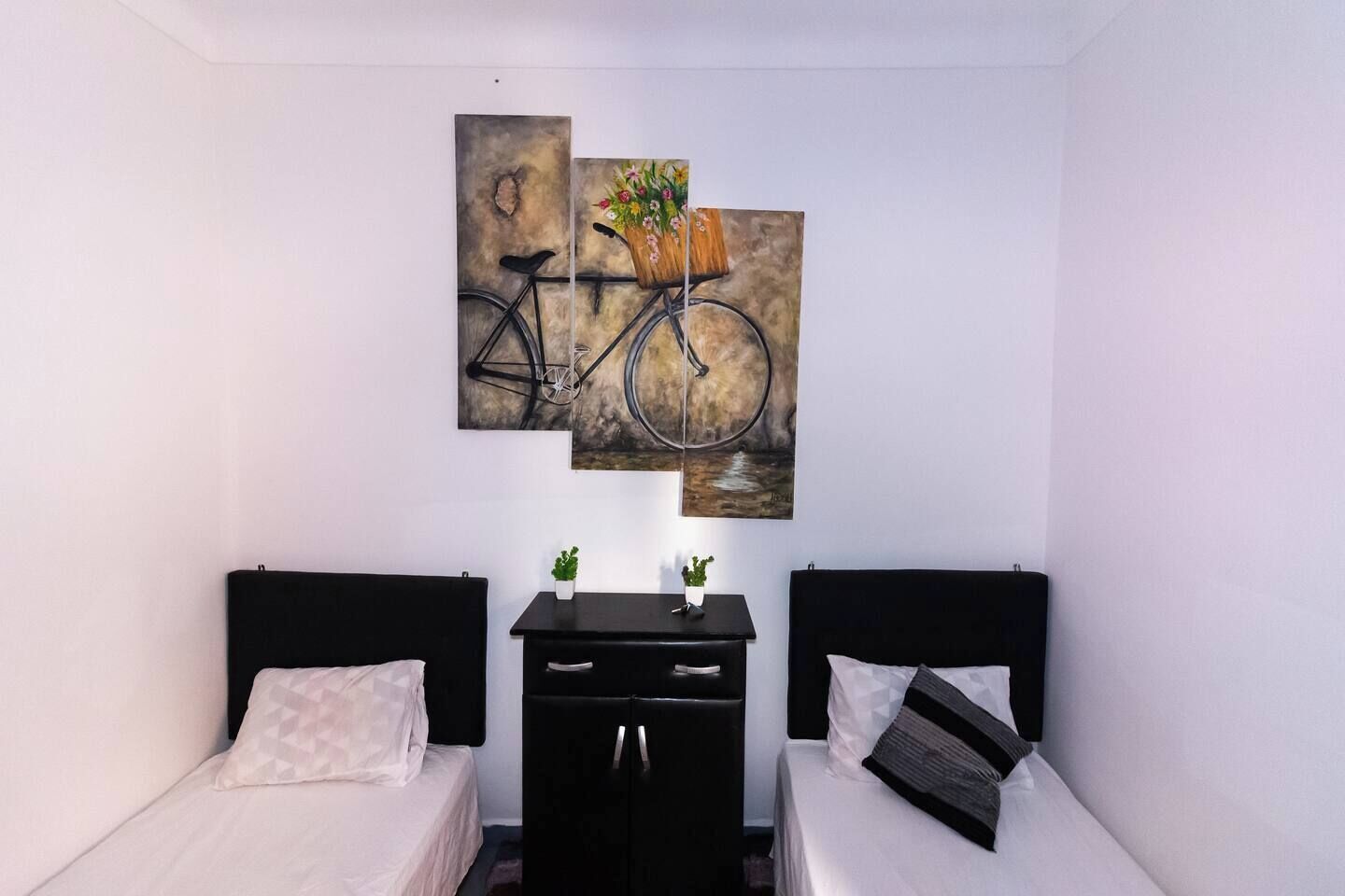 Quarto com duas camas, uma escrivaninha e um quadro na parede de uma bicicleta.