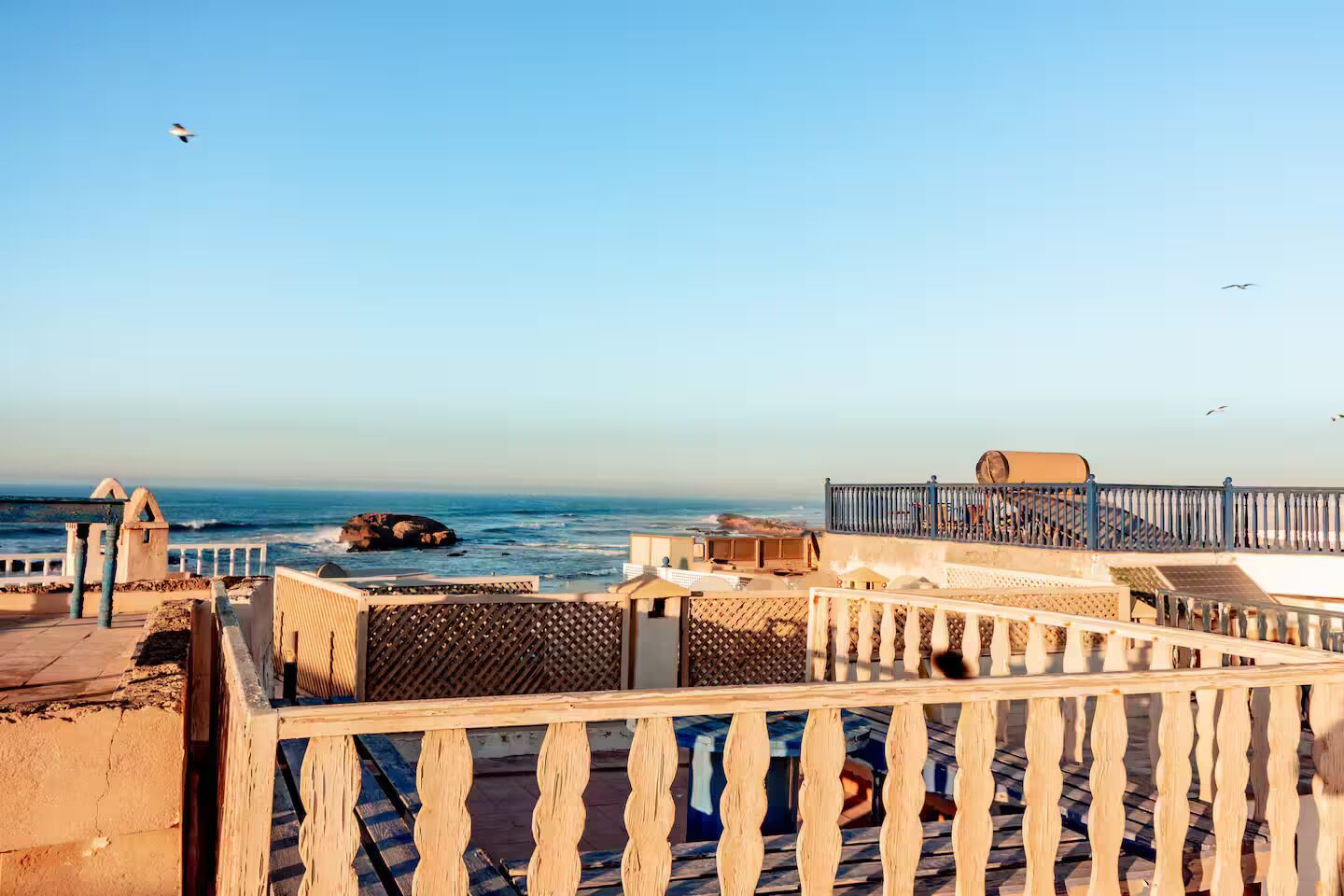 A coastal view with a wooden railing, a rocky outcrop, and a clear sky.