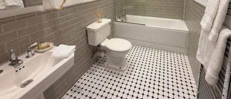 A bathroom with a white sink, toilet, and bathtub, tiled floor, and a mirror with a light fixture.