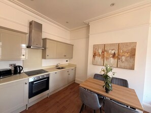 Eine moderne Küche mit Backofen, Kaffeemaschine und einem Esstisch mit Stühlen.
