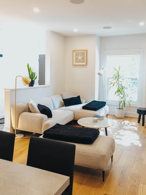 A modern living room with a sofa, a coffee table, and a dining area with chairs. - Beautiful modern 2Bdr sunny home with French decor (Hamilton)