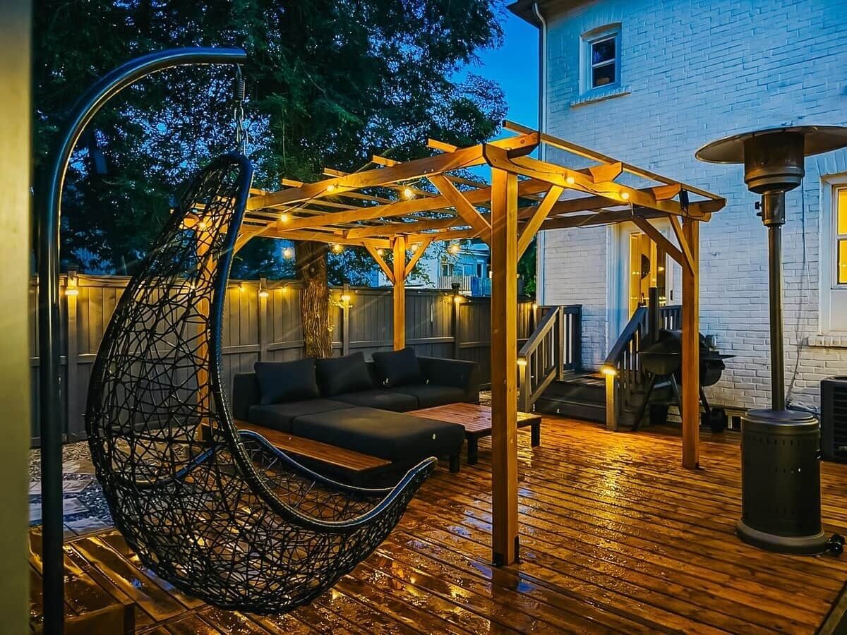 Eine Terrasse im Freien mit einem Hängesessel, einer Holz-Pergola und einem Grill.