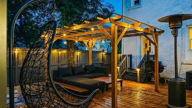 Een terras buiten met een hangstoel, een houten pergola en een barbecue.