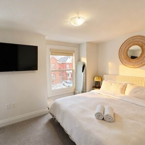 A bedroom with a bed, a flat-screen TV, a window, a mirror, and a wall-mounted light fixture. - Beautiful modern 2Bdr sunny home with French decor (Hamilton)