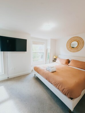A bedroom with a bed, a flat-screen TV mounted on the wall, a window, and a round mirror. - Beautiful modern 2Bdr sunny home with French decor (Hamilton)