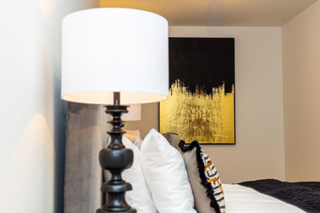 A hotel room with a bed, a lamp, and a large framed picture on the wall.