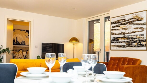 A dining area with a round table set for two, a sofa, and a television in the background. - Birmingham City Retreat No 117 (Birmingham)
