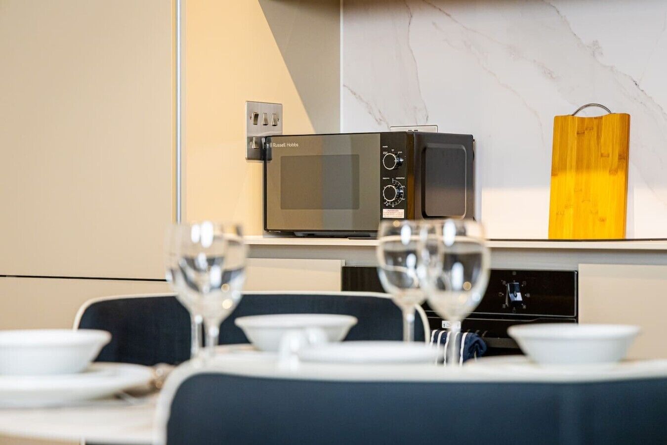 A dining area with a microwave, a wooden block, and a wine glass on a table.