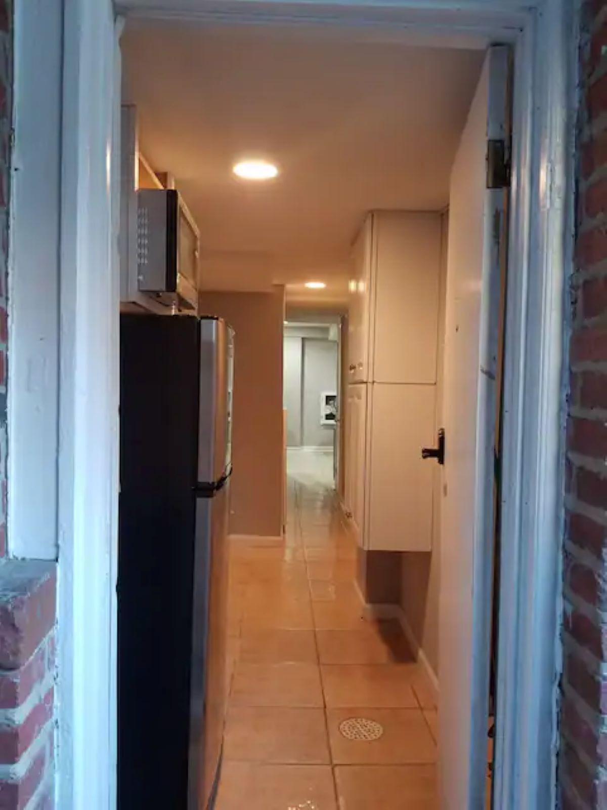 A narrow hallway with a refrigerator, cabinets, and a tiled floor.