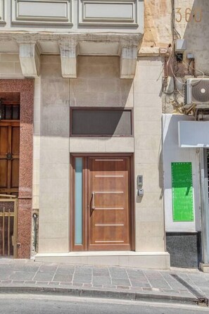 A building with a wooden door, a small window, and a green sign on the wall. - Sliema Central 1BR Apt | Own Entrance, Walk to Sea (Tas-Sliema)