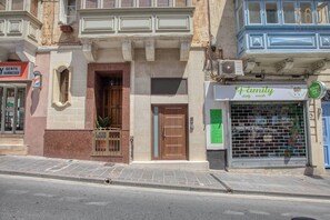 Vista de carrer amb un edifici que té una botiga amb un cartell verd, un barber amb un cartell vermell i un edifici blau amb un cartell blanc.