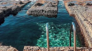 A rocky shoreline with clear water and metal steps leading into the sea. - Sliema Central 1BR Apt | Own Entrance, Walk to Sea (Tas-Sliema)