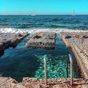 A rocky shoreline with clear water and metal steps leading into the sea. - Sliema Central 1BR Apt | Own Entrance, Walk to Sea (Tas-Sliema)