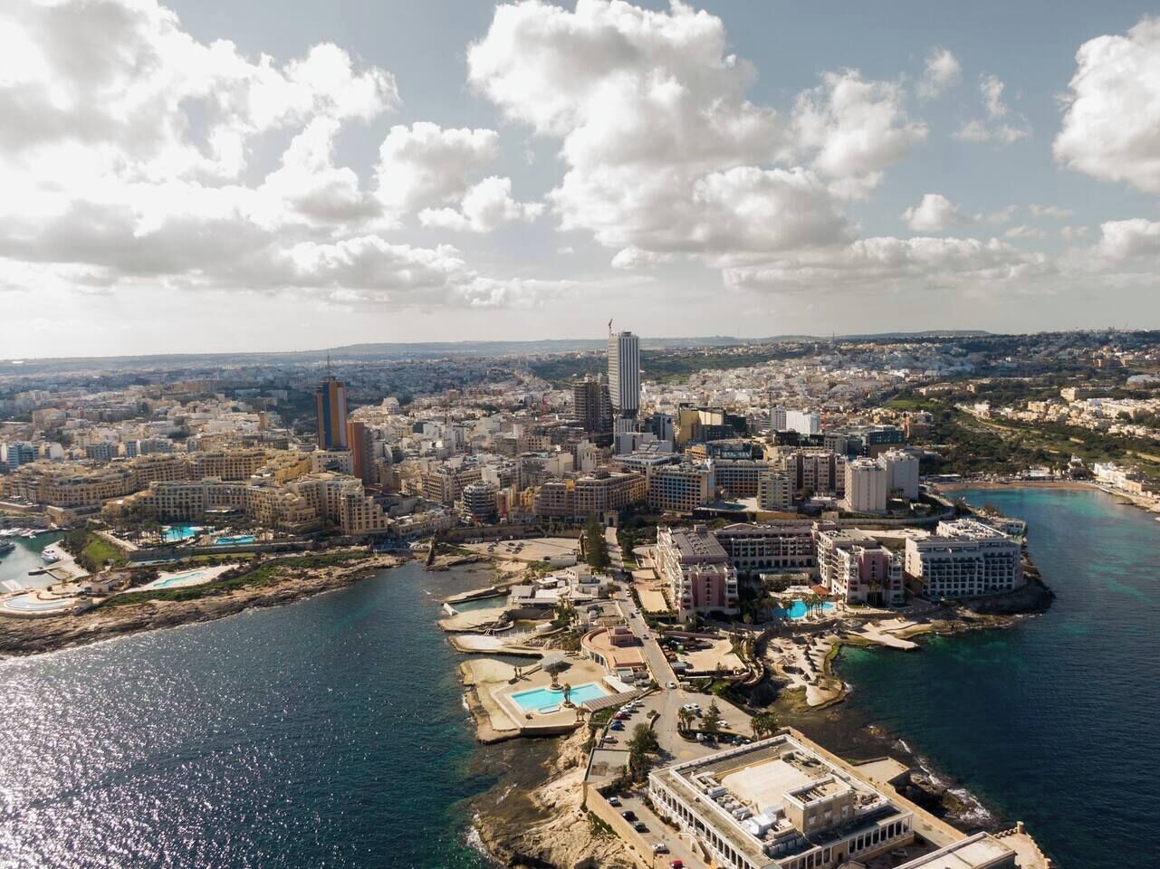 Vista aérea de una ciudad costera con un rascacielos destacado, un puerto deportivo y una zona de playa.