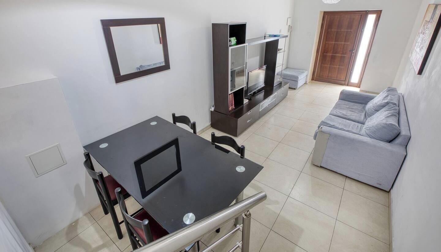 Una sala de estar con un sofá gris, un mueble para la televisión y una mesa de comedor con sillas.