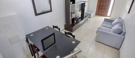 Una sala de estar con un sofá gris, un mueble para la televisión y una mesa de comedor con sillas.
