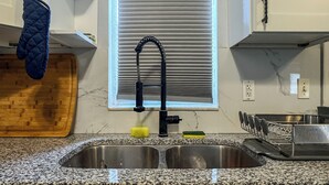 Una cocina con un lavamanos doble, armarios blancos, un ventanal con persianas y un colgador para ollas.