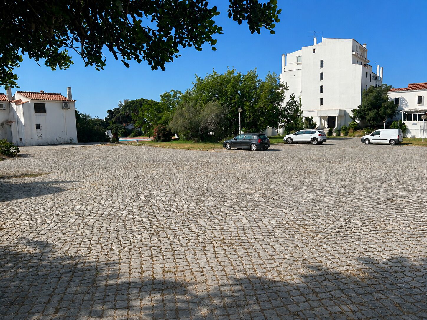 A paved parking area with multiple cars, surrounded by buildings and greenery.
