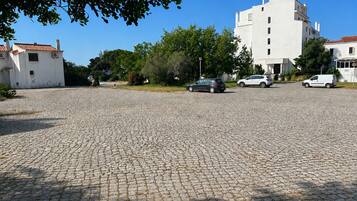 A paved parking area with multiple cars, surrounded by buildings and greenery.