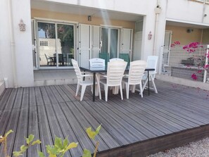 An outdoor patio with a table and chairs, a wooden deck, and a view of a building with shutters. - CALVI 2-bedroom apartment with a garden (Calvi)