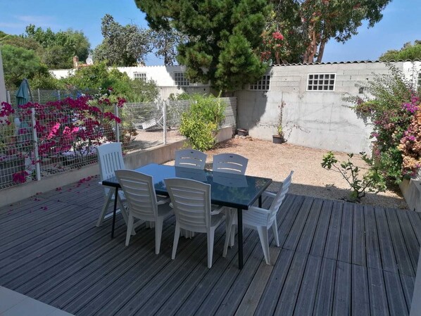 Un patio exterior con una mesa y sillas, rodeado por un jardín con diversas plantas y flores.