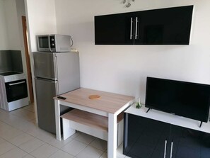 Eine kompakte Küche mit Mikrowelle, Kühlschrank, Backofen und einem kleinen Tisch mit Fernseher.