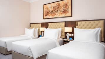 A hotel room with three beds, a wall-mounted artwork, and a nightstand with a lamp.