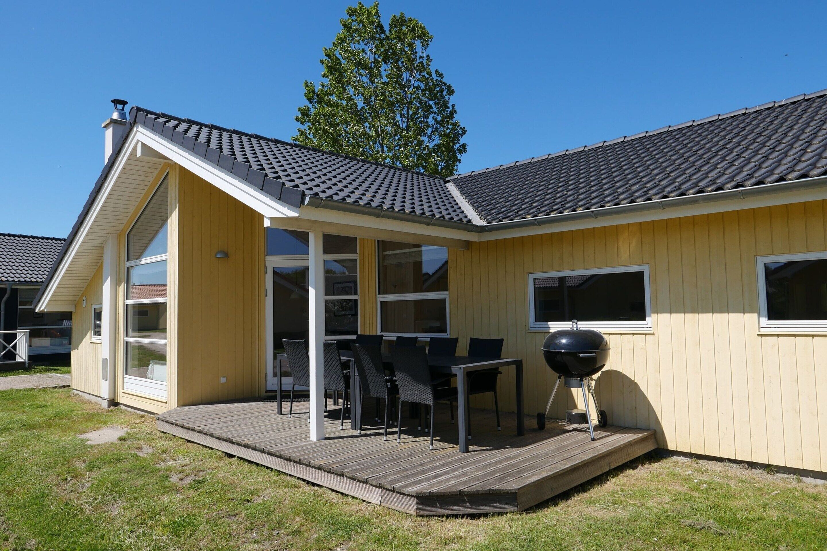 Ein eingeschossiges Haus mit überdachter Terrasse, Grill und großem Fenster.