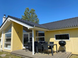 A yellow building with a covered patio, a grill, and a large window.