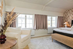 Una habitació amb llit, cadira, taula i finestra amb cortines.