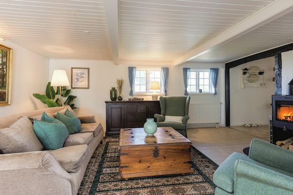 A living room with a sofa, armchair, coffee table, and a fireplace. - Half-timbered cottage near Knuthenborg Park (Maribo)